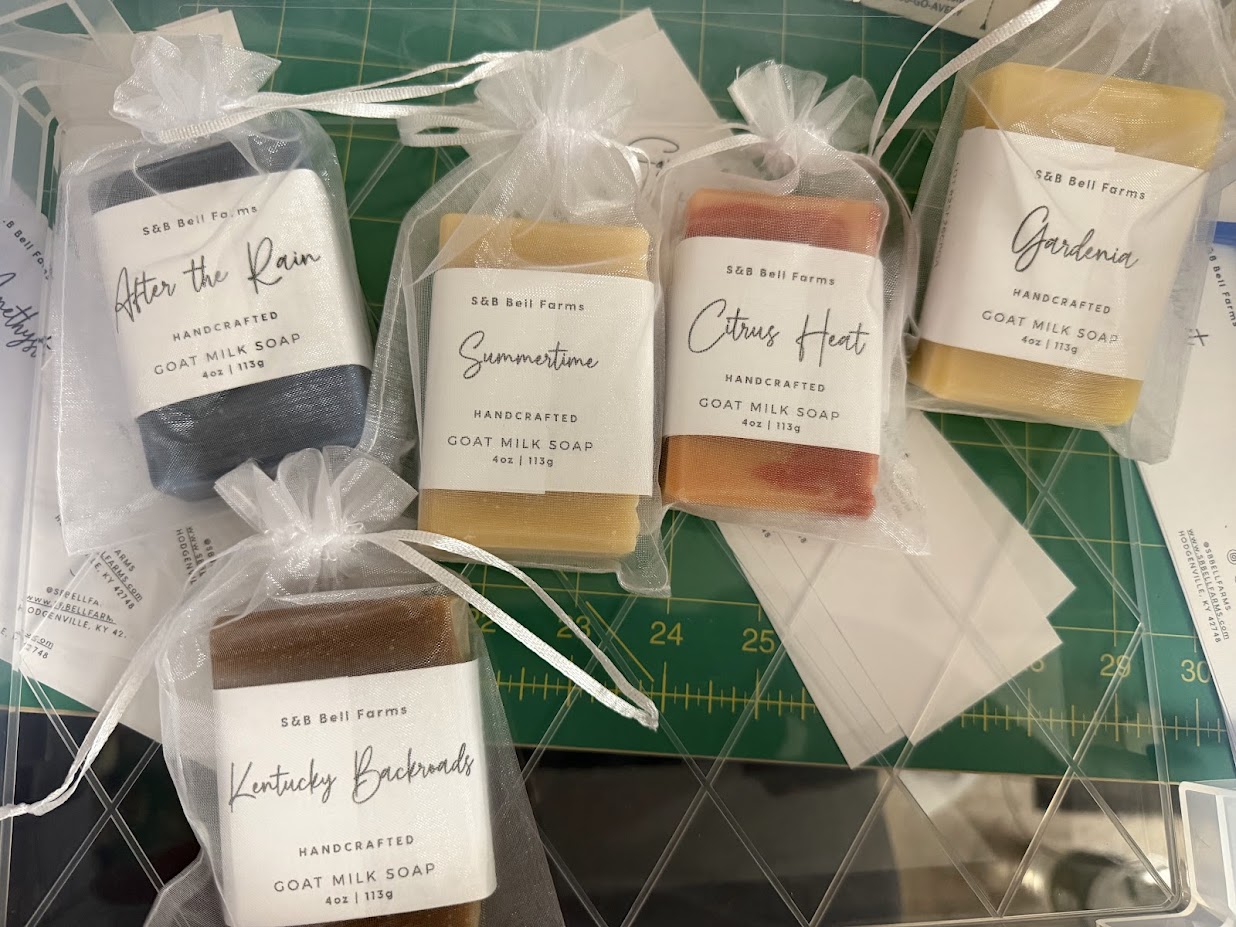 Several bars of packaged handmade goat milk soap on a table, each wrapped and labeled, showcasing a variety of scents.